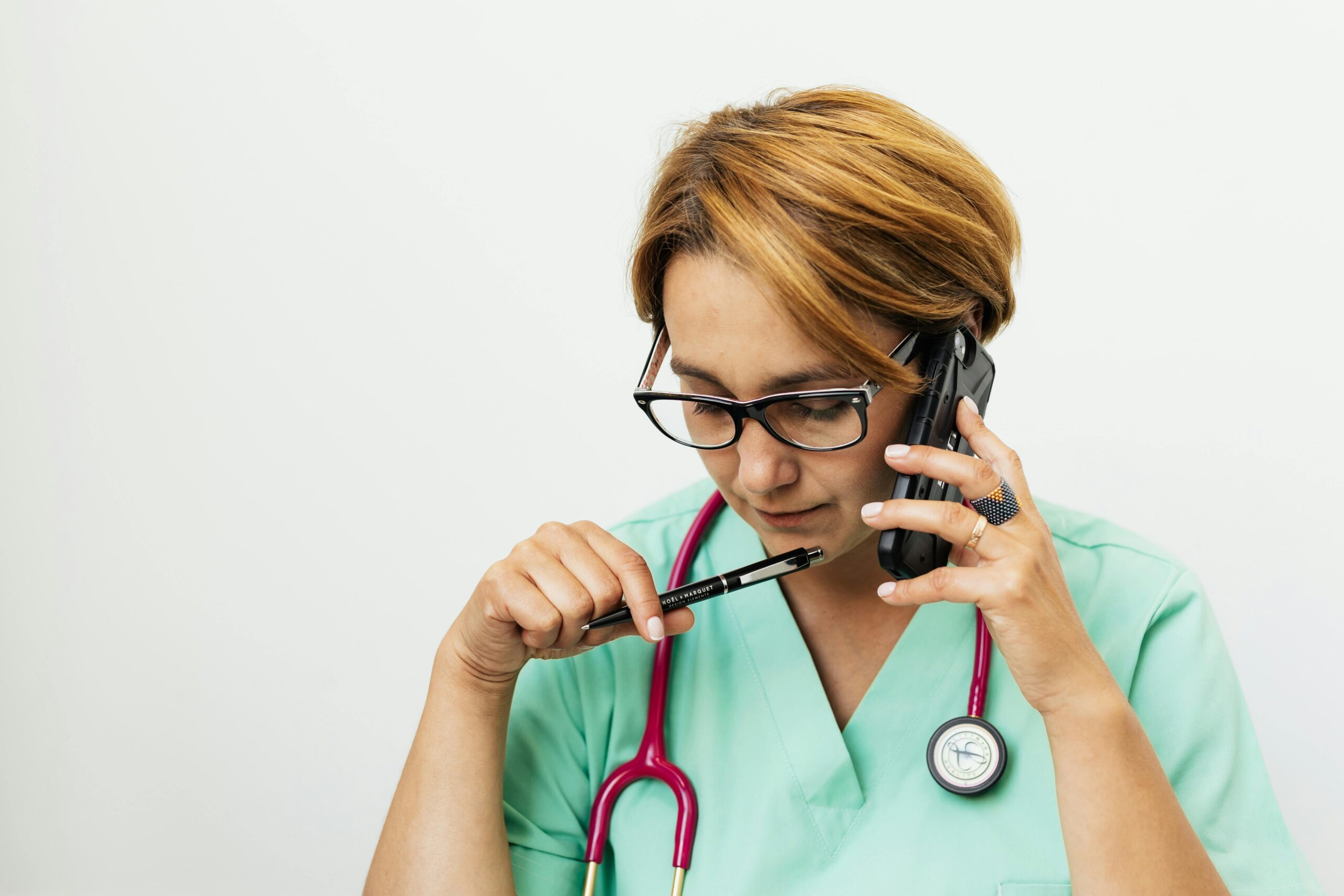 Focused female doctor with eyeglasses and stethoscope talking on the phone for medical consultation.