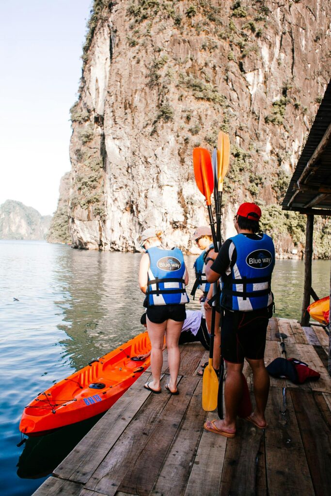 Group of adults preparing for kayaking on a picturesque lake surrounded by cliffs.